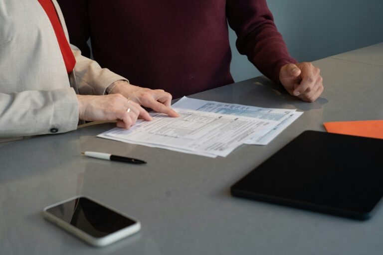 Person reviewing an insurance declaration page, policy booklet, and calculator on a kitchen table.